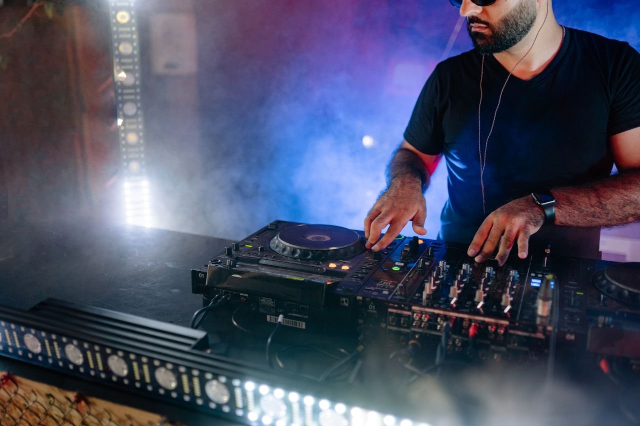 Energetic DJ performing live with mixing equipment in a colorful nightclub setting.