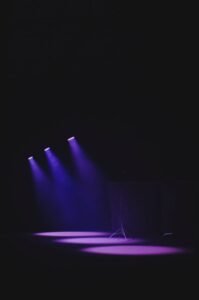 Moody theater scene with purple spotlights casting a vivid glow on an empty stage.